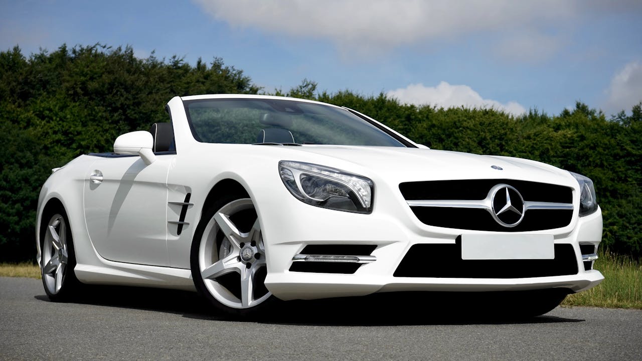Stunning white Mercedes Benz convertible parked on the road against a lush green backdrop.